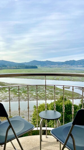 A balcony with two chairs and a table, overlooking a river and distant hills. - The Cliffs - Galician Blue Views (Ortigueira)