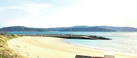 A beach with a rocky breakwater, a small wooden structure, and a parked car.