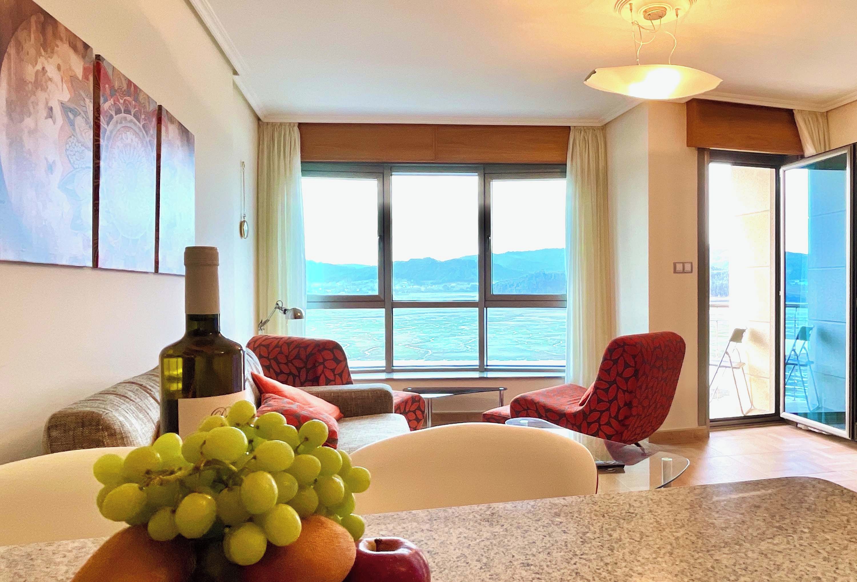 A room with a large window, a bottle of wine, and a fruit bowl.