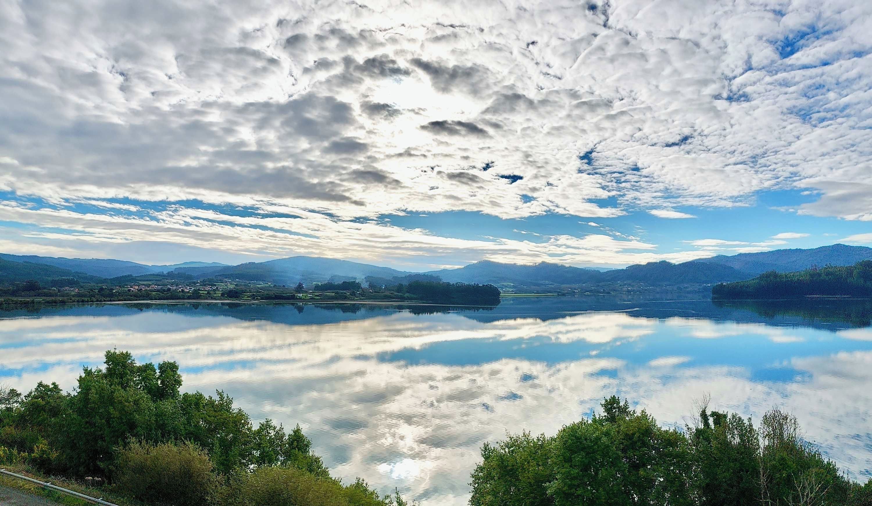 A calm lake with a clear reflection of the sky and surrounding landscape.