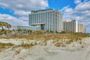 Un hotel frente a la playa con varios edificios altos, una playa de arena y palmeras.