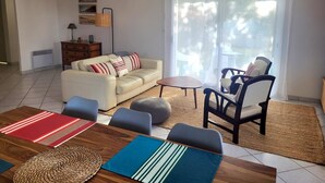 A living room with a sofa, chairs, a coffee table, and a dining table with placemats. - A relaxing break in the heart of the Basque Country (Ascain)