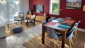 A modern living room with a red accent wall, a dining area with a wooden table and chairs, and a television on a wooden cabinet. - A relaxing break in the heart of the Basque Country (Ascain)