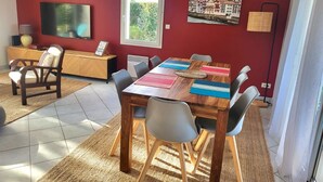 A dining area with a wooden table, six chairs, and a red wall with a window and artwork. - A relaxing break in the heart of the Basque Country (Ascain)