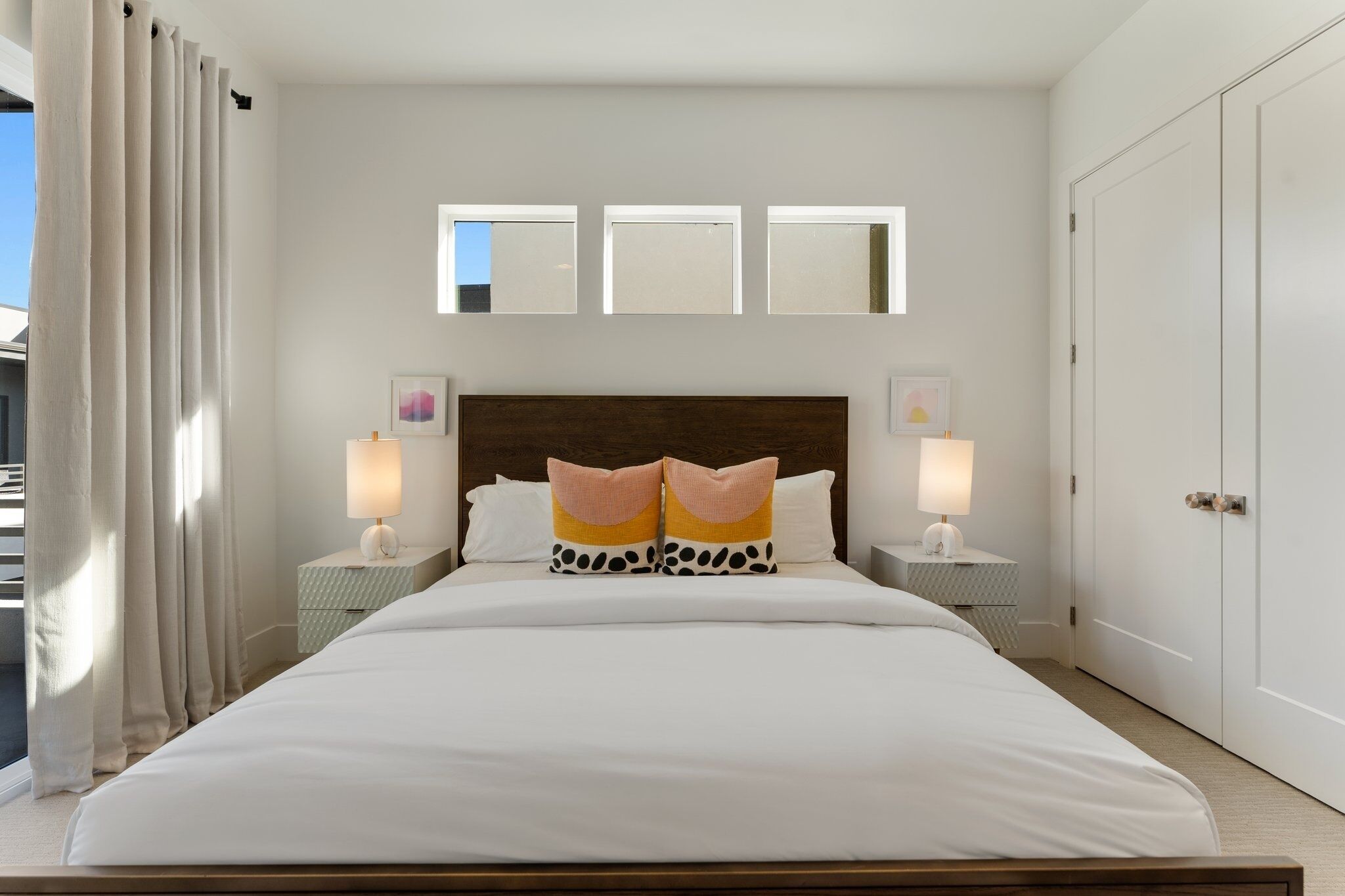 A hotel room with a large bed, two bedside tables with lamps, a headboard with a mirror, and a wardrobe.