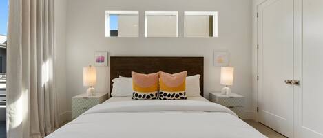 A hotel room with a large bed, two bedside tables with lamps, a headboard with a mirror, and a wardrobe.
