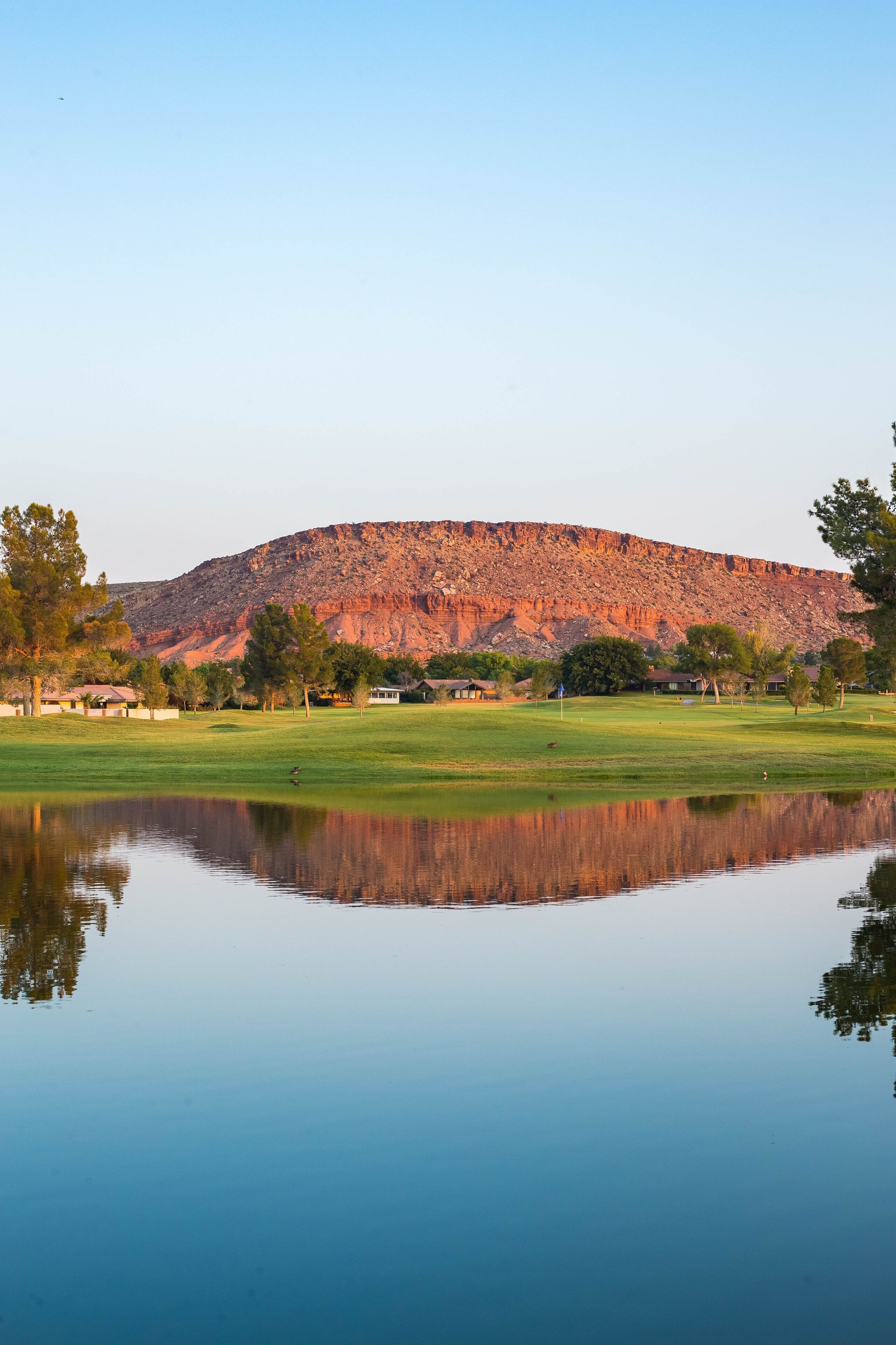 A tranquil golf course with a clear reflection in the water, surrounded by trees and a mountain in the background.