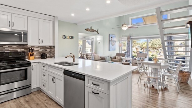 Une cuisine moderne avec des meubles blancs, une cuisinière en acier inoxydable et un lave-vaisselle. On y trouve également un coin repas avec une table et des chaises blanches.