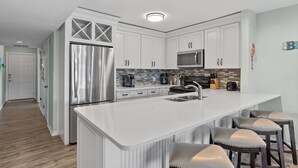 Une cuisine moderne avec des meubles blancs, des appareils en acier inoxydable et un îlot central doté de tabourets de bar.