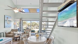 Un salon spacieux doté d’un ventilateur de plafond, d’un grand téléviseur et offrant une vue sur l’extérieur.