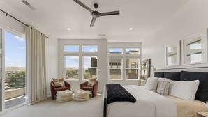 Un dormitorio amplio con una cama grande, un ventilador de techo y vistas a la ciudad a través de amplias ventanas.