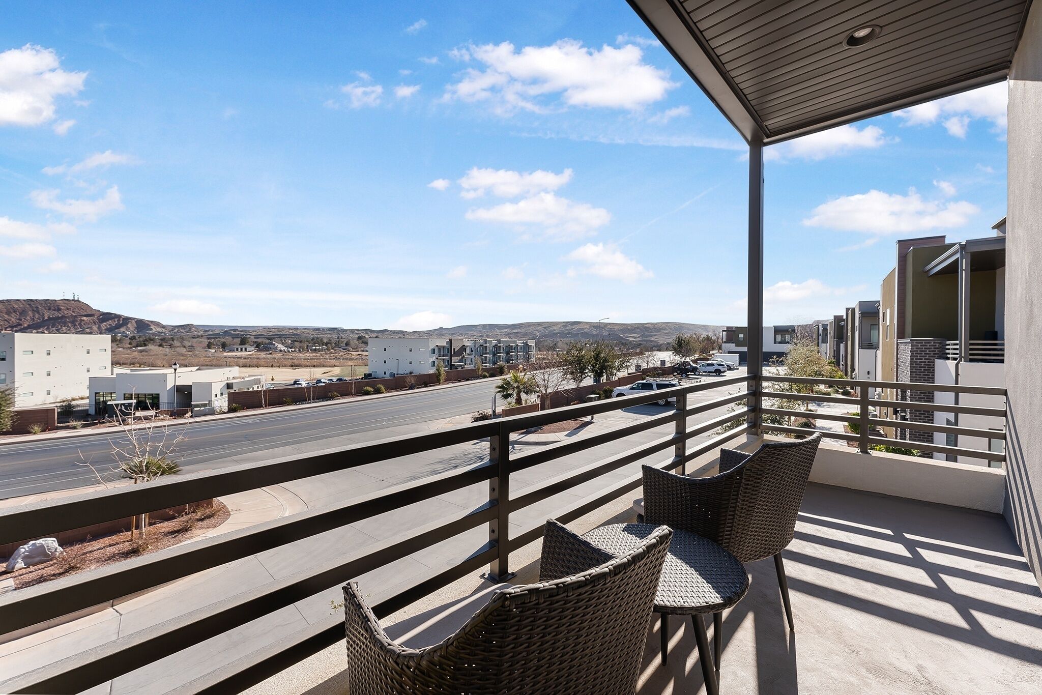 A balcony with wicker furniture overlooking a road and distant hills.