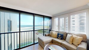 Ein Balkon mit Blick auf Strand und Meer, eine Couch mit gemusterten Kissen und ein runder Couchtisch.