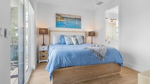 Quarto com uma cama grande, um quadro acima da cama e vista para o exterior por uma janela ampla.
