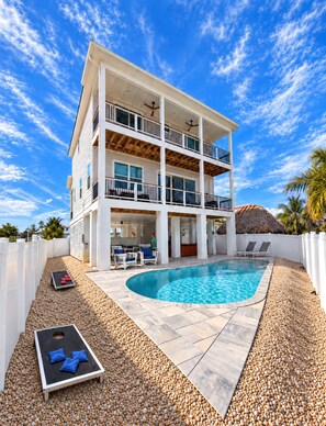 A multi-story building with a swimming pool, outdoor seating, and a thatched-roof structure. - 118 Fairweather Ln - Brand New 4 Bed+den/4.5 Bath Home W.hot Tub 4 Bedroom Home (Fort Myers Beach)