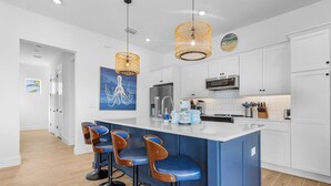 Uma cozinha moderna com armários brancos, uma ilha azul com banquetas e iluminação pendente.