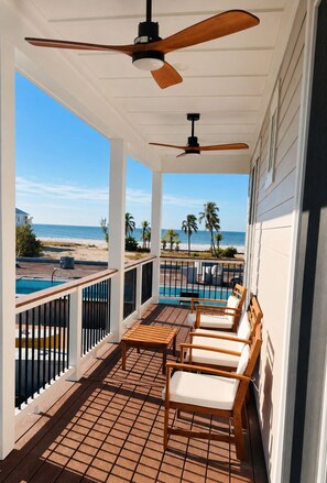 A covered outdoor area with a pool, wooden chairs, and a view of the beach. - 118 Fairweather Ln - Brand New 4 Bed+den/4.5 Bath Home W.hot Tub 4 Bedroom Home (Fort Myers Beach)