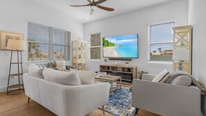Uma sala de estar moderna com um sofá, uma mesa de centro e uma televisão exibindo uma cena de praia.
