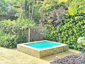 Relax by the rectangular pool surrounded by lush greenery and a stone border.
