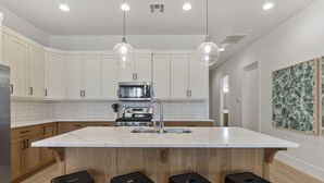 A modern kitchen with white cabinets, a large island with stools, stainless steel appliances, and pendant lighting. - Villa #12 At Bloomington Country Club 4 Bedroom Townhouse (St. George)
