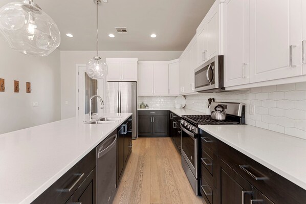 A modern kitchen with white cabinets, a stainless steel refrigerator, a microwave, a stove, and a large island with a sink. - Villa #01 At Bloomington Country Club 3 Bedroom Condo (St. George)