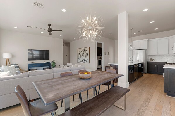 A modern living room with a large sofa, a dining table, and a kitchen in the background. - Villa #01 At Bloomington Country Club 3 Bedroom Condo (St. George)