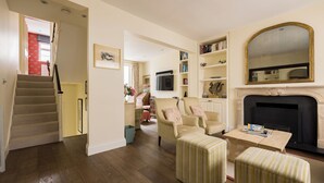 A spacious living room with a fireplace, a staircase, and a bookshelf. - The Chelsea Abode - 4bdr Home With Terrace (London)