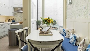 A kitchen with white cabinets, a dining table with blue cushions, and a window with a view. - The Chelsea Abode - 4bdr Home With Terrace (London)