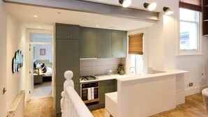 A modern kitchen with a central island, built-in appliances, and a view into the adjacent bedroom. - The Kensal Green Hideout - Classy 2bdr Apartment (London)