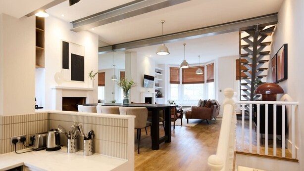 A modern kitchen with a dining area, wooden flooring, and a staircase leading to an upper level. - The Kensal Green Hideout - Classy 2bdr Apartment (London)
