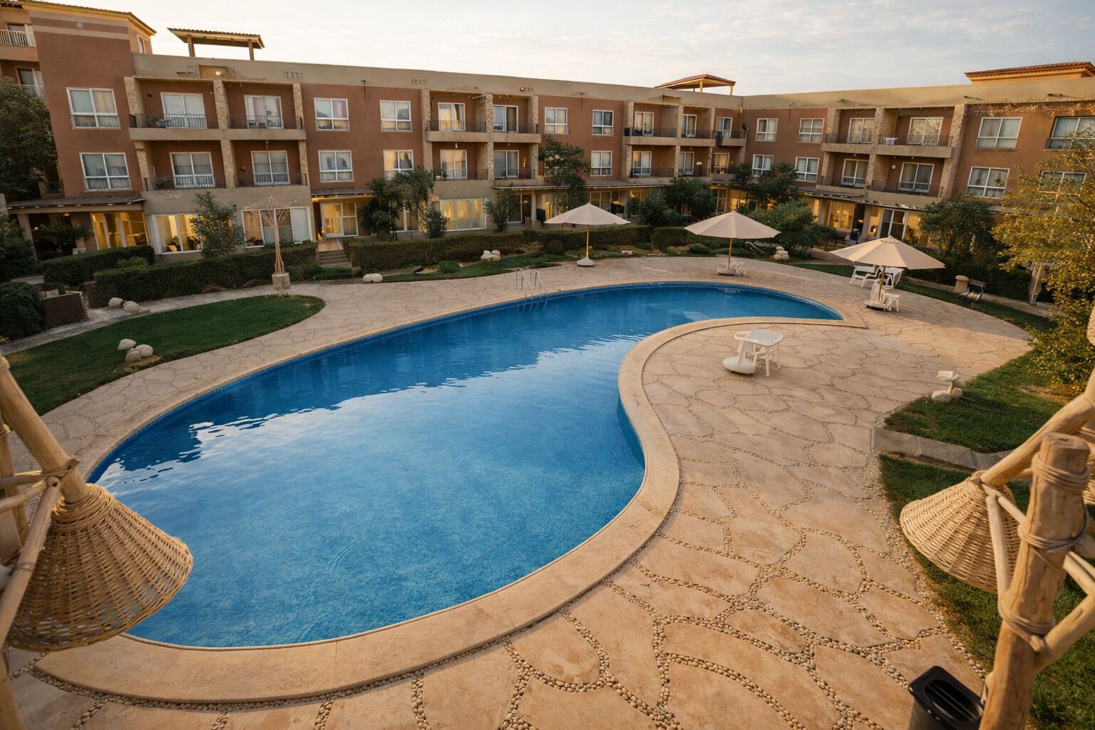 A swimming pool with a curved edge, surrounded by a stone deck. There are lounge chairs and umbrellas around the pool.