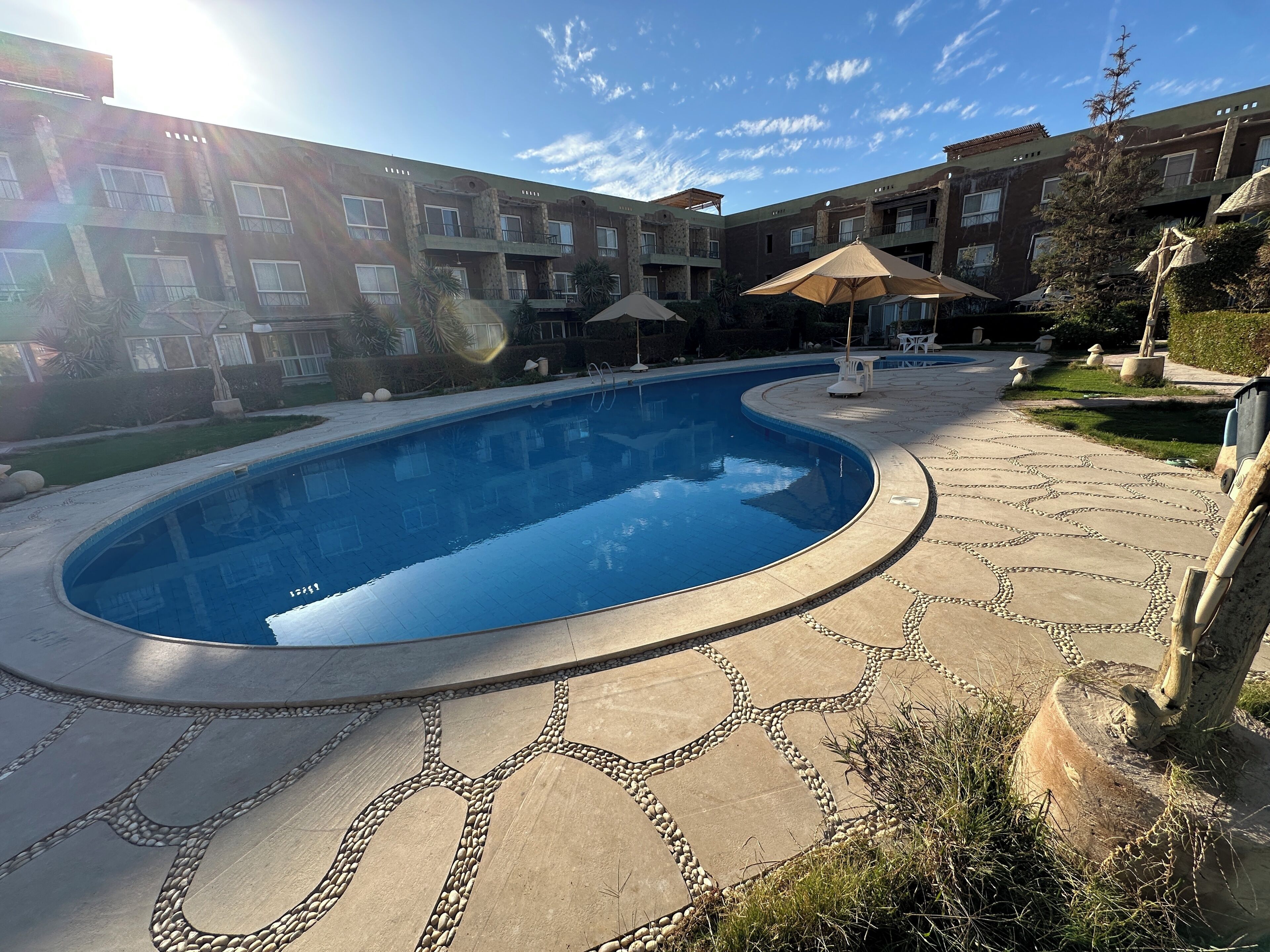 A swimming pool with a stone pathway, surrounded by a multi-story building with balconies.