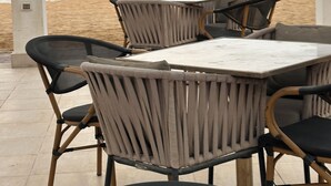 An outdoor dining area with wicker chairs and a table, overlooking a beach and the sea. - Cozy Chalet With Stunning View  (Ataqah)