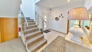 Et moderne interiør med trappe, tremmer i glas, en trädør, en dekorativ lampe og en lille plante.
