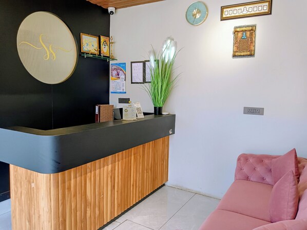 A reception area with a wooden reception desk, a pink sofa, and various framed items on the wall. - Serenity Suites (Ootacamund)