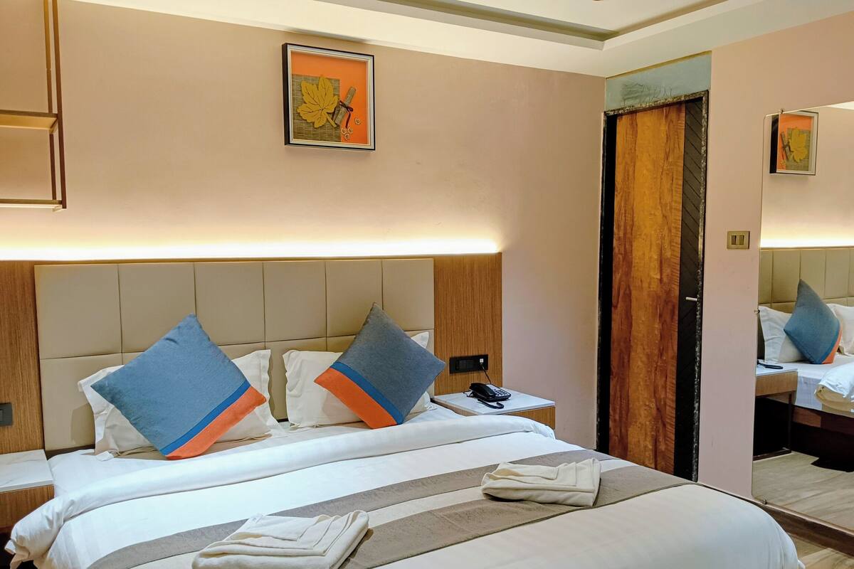 Una habitación de hotel con una cama grande, dos mesitas de noche, un teléfono junto a la cama y un espejo.