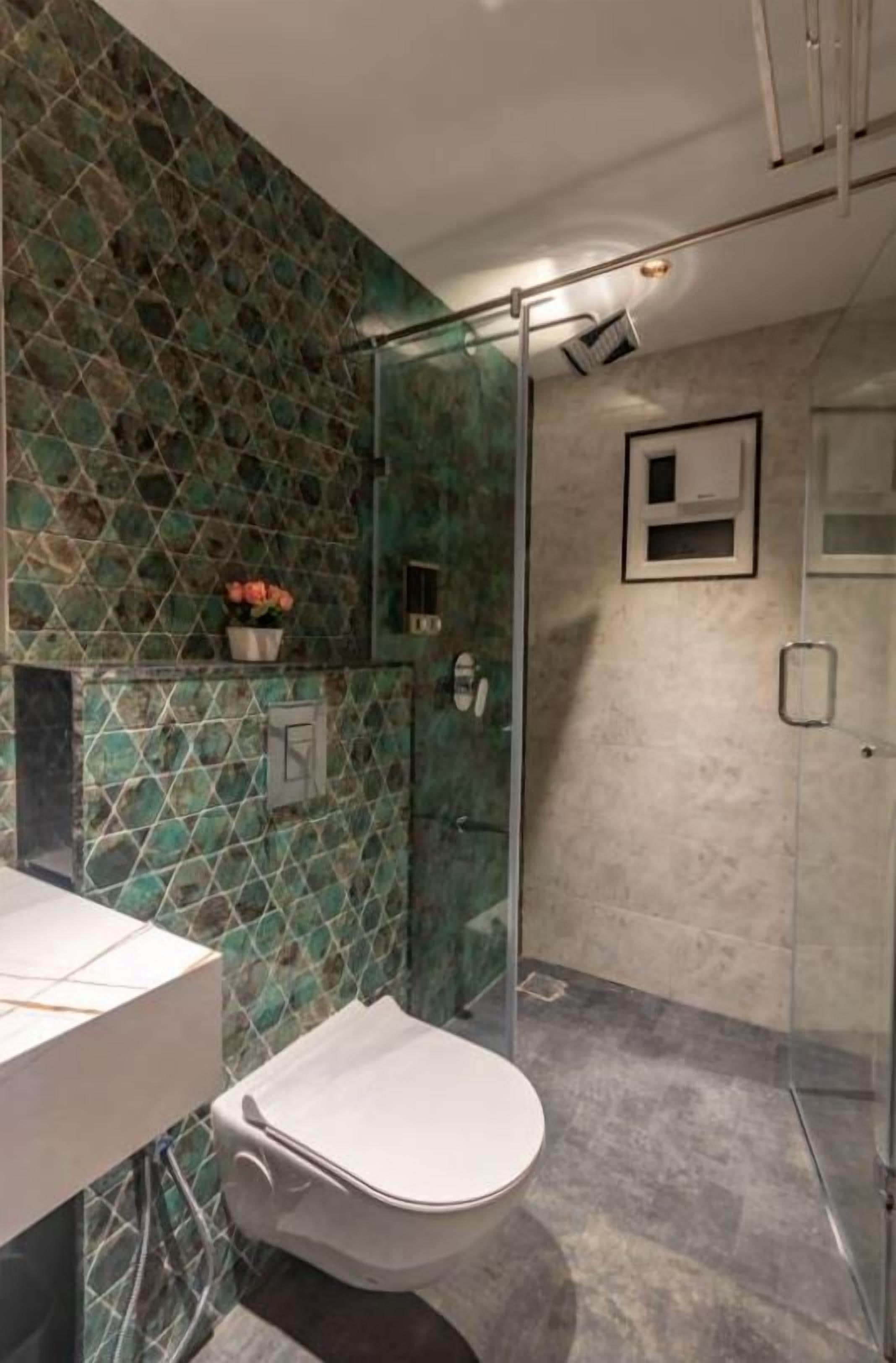 Et moderne badeværelse med en glasbrusekabine, et hvidt toilet og en flisevæg med et geometrisk mønster.