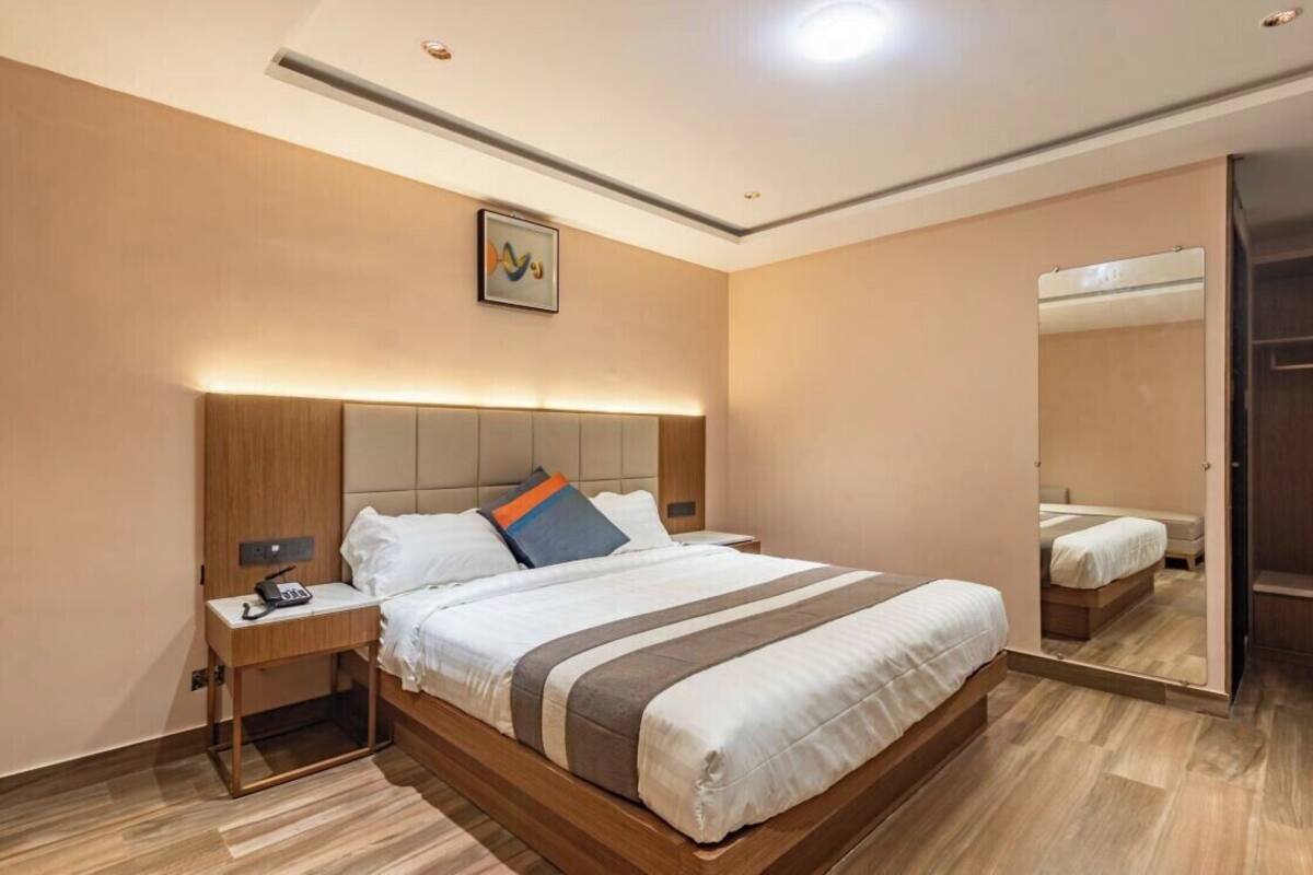 Una habitación de hotel moderna con una cama grande, mesitas de noche, un espejo y una lámpara en el techo.