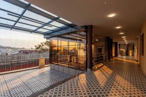 A spacious corridor with patterned flooring, a glass enclosure with a view of the city, and a metal railing along the side. - Serenity Suites (Ootacamund)