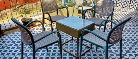 A terrace with a table and four chairs, a patterned floor, and a view of a red building in the background.