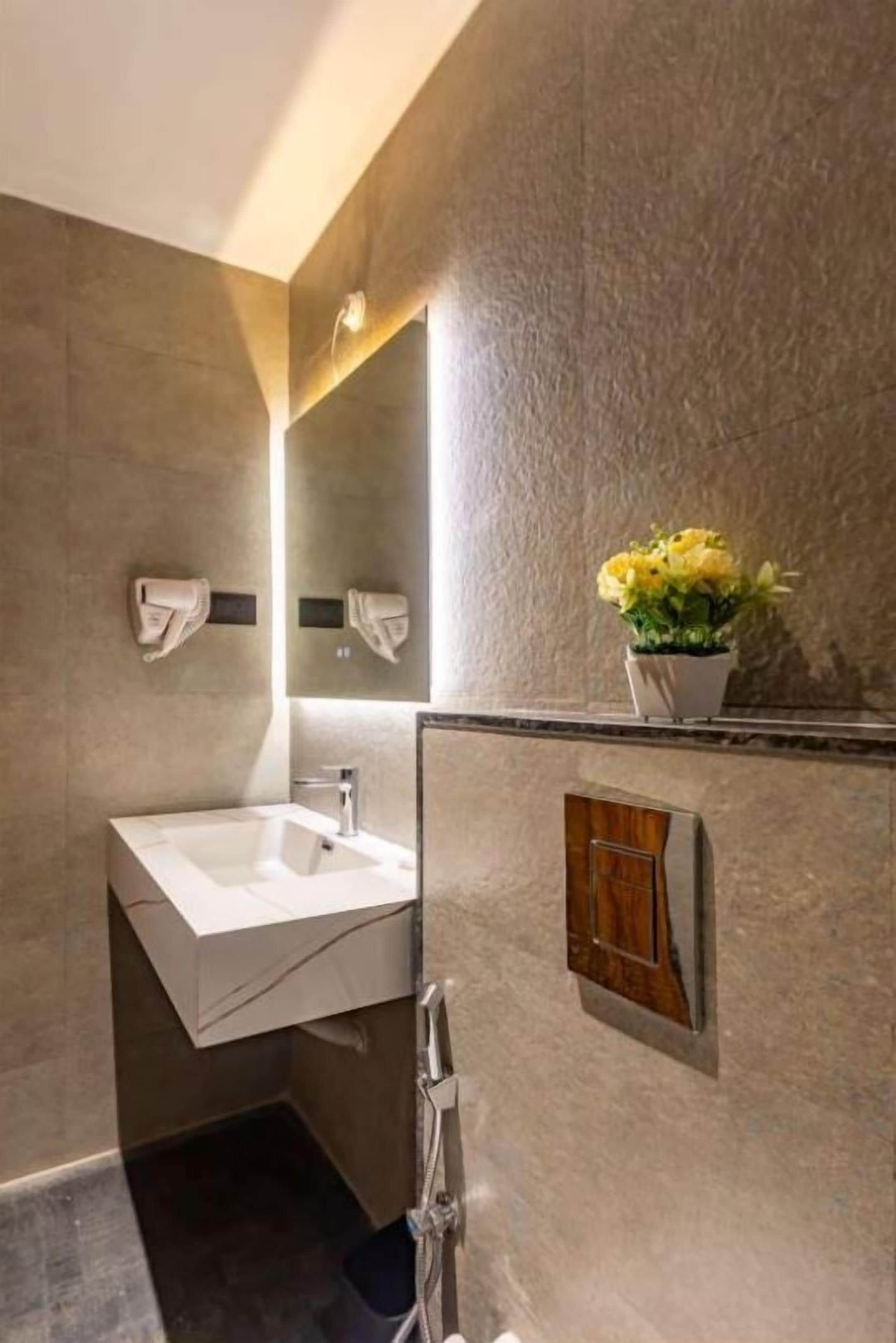 Een moderne badkamer met een wit wastafel, douche en spiegel. Een potplant met gele bloemen staat op de muur.