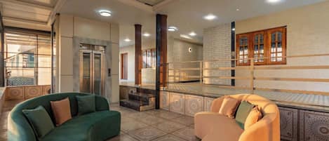 A spacious lobby with a curved green sofa and a beige armchair, a staircase, and a patterned floor.
