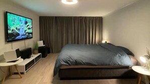 Moderni makuuhuone, jossa on sänky, televisio, työpöytä ja pieni sivupöytä.