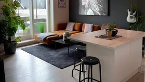 Moderni olohuone, jossa on suuri ikkuna, sohva, sohvapöytä ja keittiösaareke.