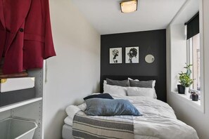 Ένα υπνοδωμάτιο με ένα κρεβάτι, ένα προσκέφαλο, ένα παράθυρο και έναν τοίχο με δύο φωτογραφίες σε κορνίζες.