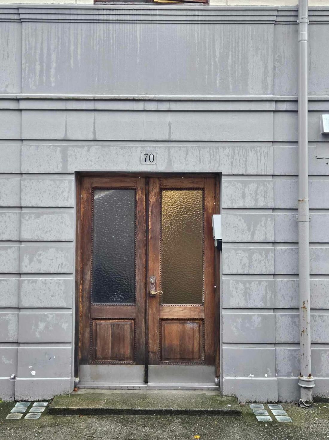 Una porta in legno a due ante con un pannello di vetro, contrassegnata dal numero 70, incastonata in una facciata di un edificio grigio.