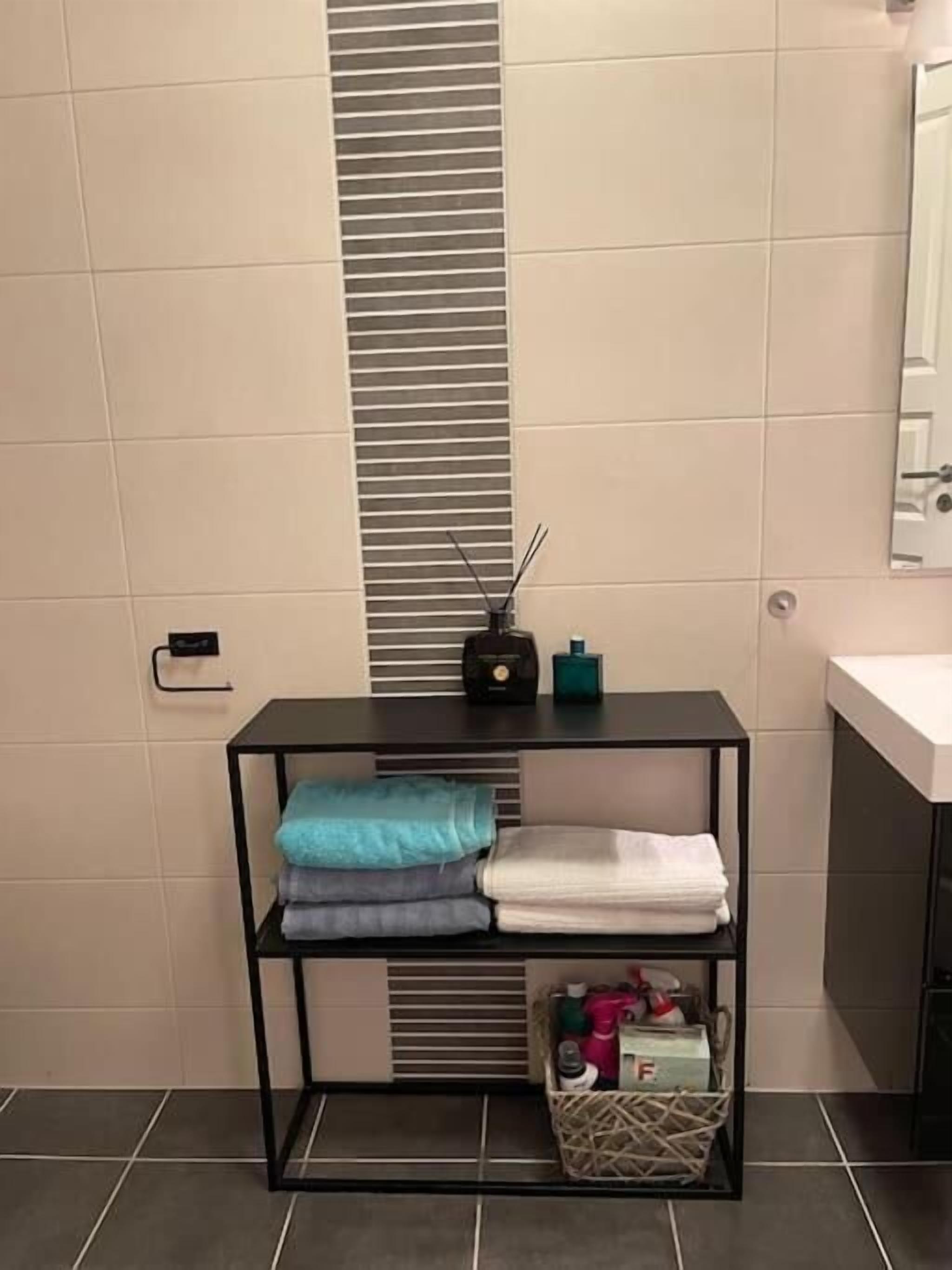 Une salle de bain avec une étagère en métal noir où sont pliées des serviettes, une petite radio et un panier contenant des articles de toilette.