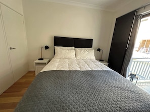 Une chambre à coucher comprenant un lit, deux tables de chevet avec des lampes, une armoire et un balcon aménagé avec du mobilier d’extérieur.
