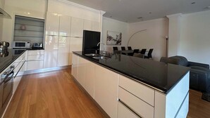 A modern kitchen with a central island, built-in appliances, and a dining area with a table and chairs. - Spacious 3 BDR family home with Parking and BBQ! (Perth)