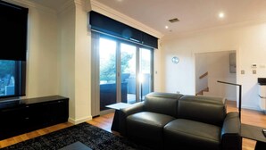 A living room with a black leather sofa, a flat-screen TV, and a sliding glass door leading to a balcony. - Spacious 3 BDR family home with Parking and BBQ! (Perth)